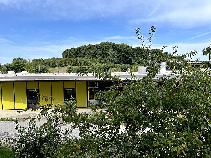 Biberkor Ansicht der Grundschule im Grünen mit Bäumen und Hügel